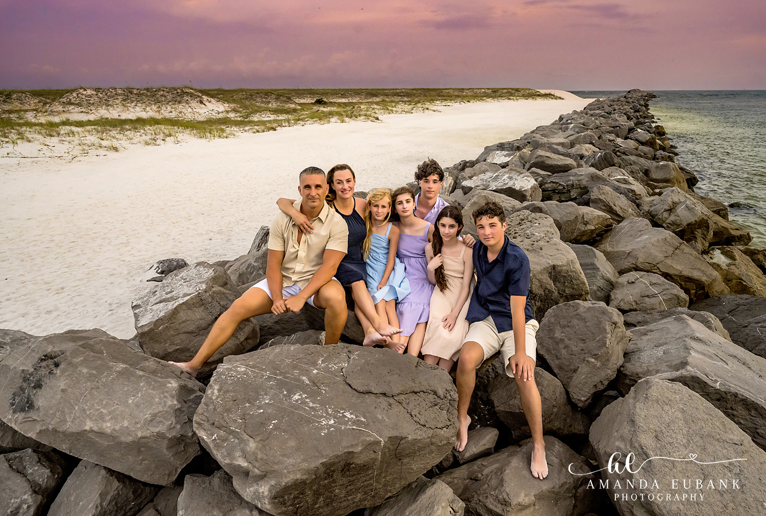 A group of kids posing together on the rocks at the Destin Jetties in Destin, Florida at sunset, photographed by Destin family photographer Amanda Eubank