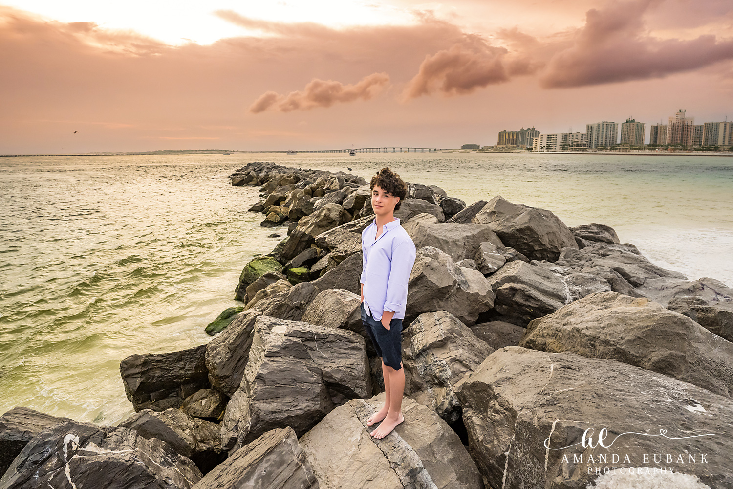 Destin Jetties Family Photos | Teen boy standing A teen boy standing on the rocks at the Destin Jetties in Destin, Florida at sunset, photographed by Destin family photographer Amanda Eubank