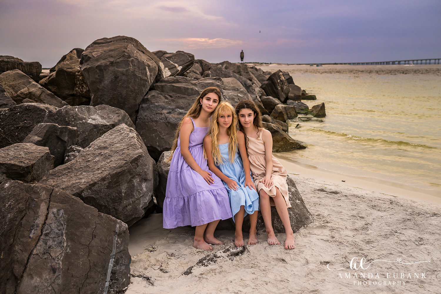 Destin Jetties Family Photos | Three girls sitting by the water Three girls sitting by the water on the rocks at the Destin Jetties in Destin, Florida at sunset, photographed by Destin family photographer Amanda Eubank