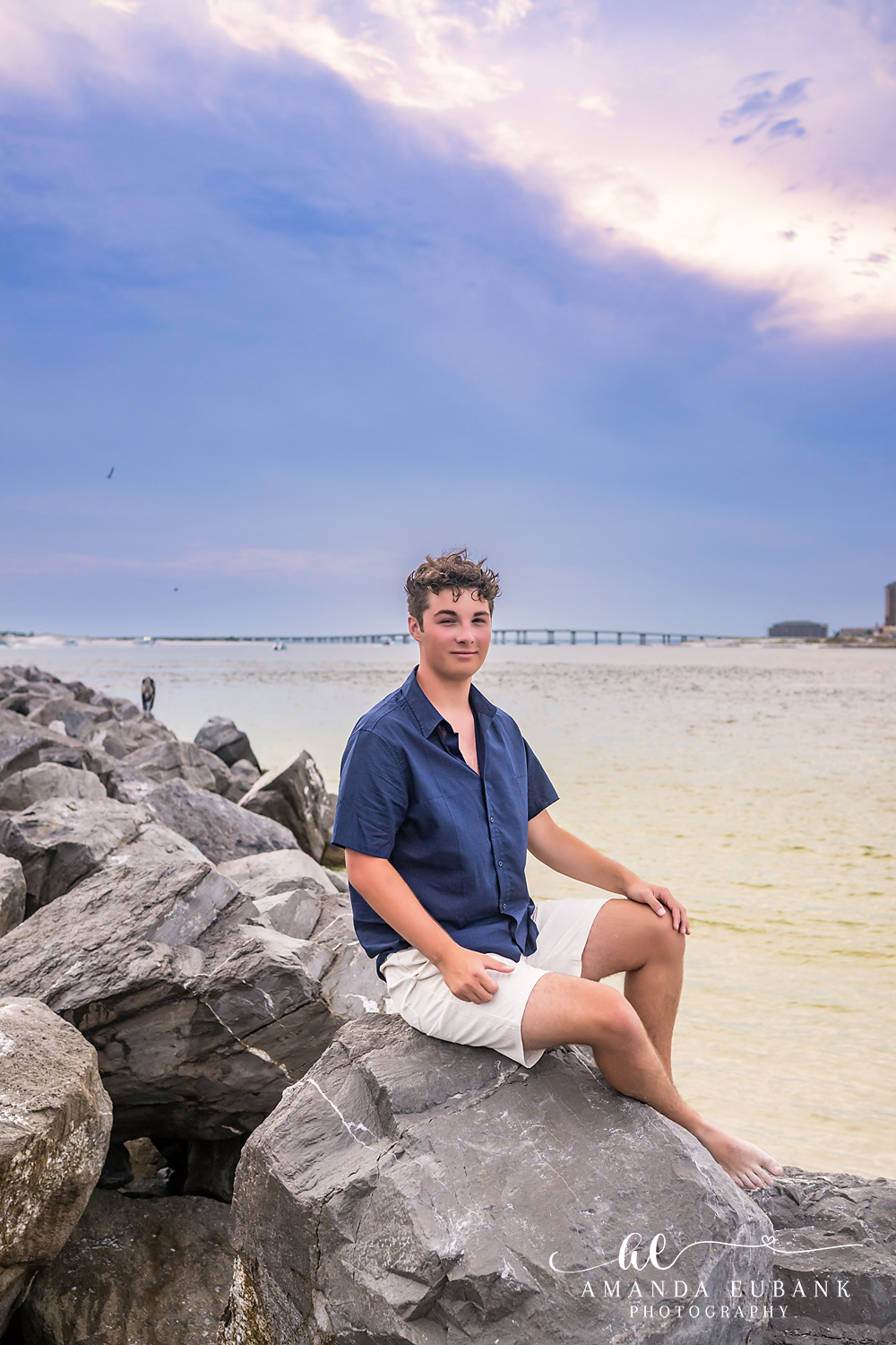 Destin Jetties Family Photos | Teen boy sitting 2 A teen boy sitting on the rocks at the Destin Jetties in Destin, Florida at sunset, photographed by Destin family photographer Amanda Eubank