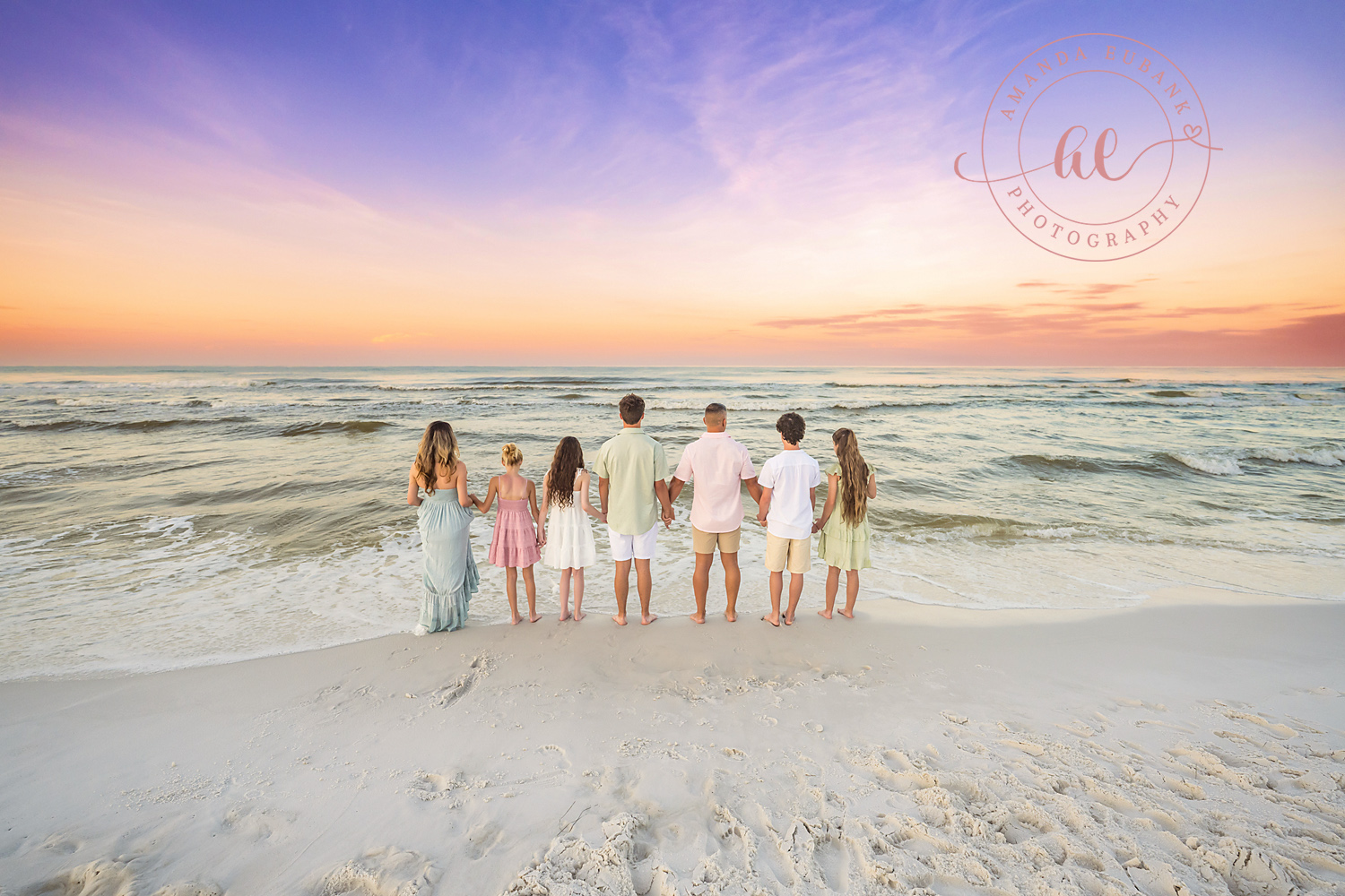 Miramar Beach Sunrise Family Photos | Family standing arm in arm facing the water A family standing arm in arm facing the water on the beach in Miramar Beach, Florida at sunrise, photographed by Miramar Beach family photographer Amanda Eubank