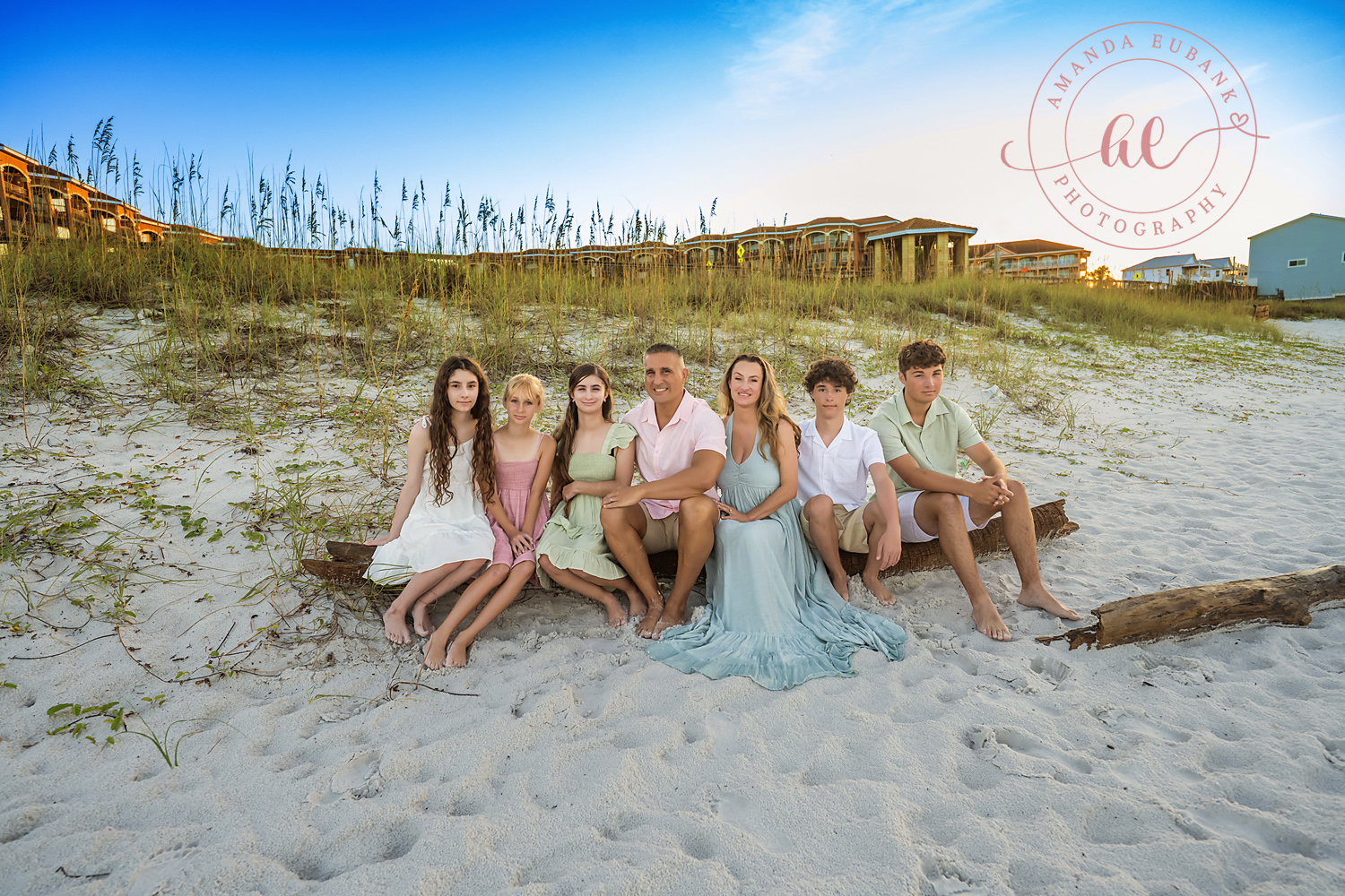 Miramar Beach Sunrise Family Photos | Family sitting among the sand dunes A family sitting among the sand dunes on the beach in Miramar Beach, Florida at sunrise, photographed by Miramar Beach family photographer Amanda Eubank