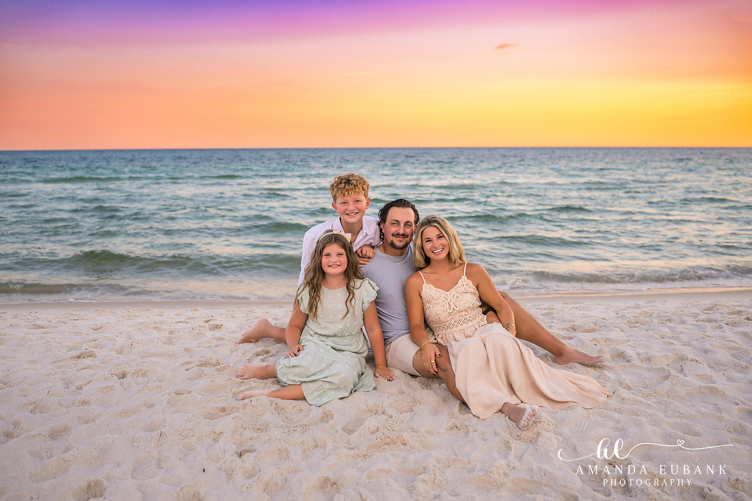 Rosemary Beach Family Photos | Family of four sitting in the sand A family of four sitting in the sand on the beach in Rosemary Beach, Florida at sunset, photographed by Rosemary Beach family photographer Amanda Eubank
