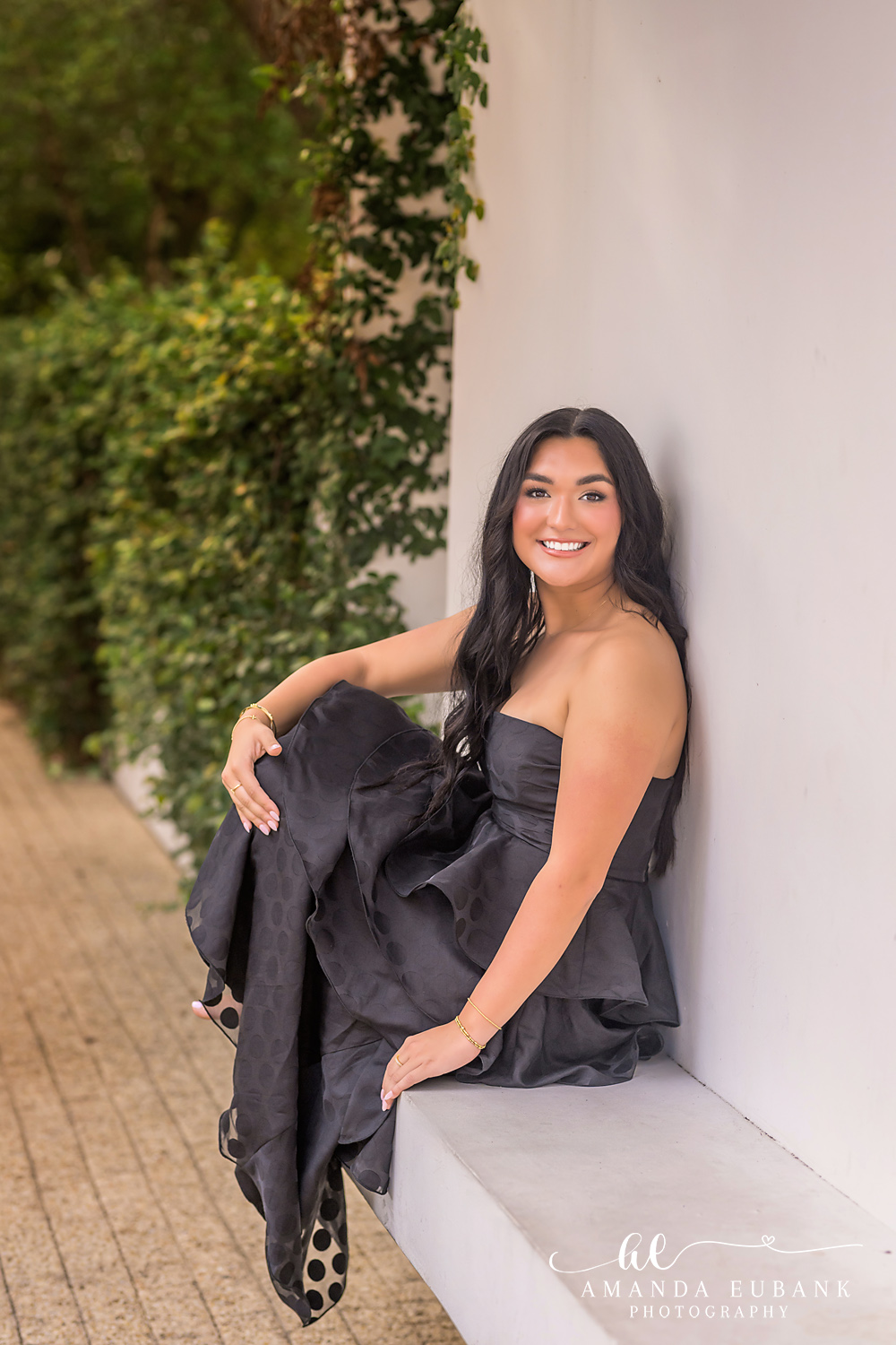 Rosemary Beach Senior Photos | Seated on a white stucco ledge Rosemary Beach senior photographer: senior girl in a black tiered dress seated on a white stucco ledge with one knee raised beside climbing ivy