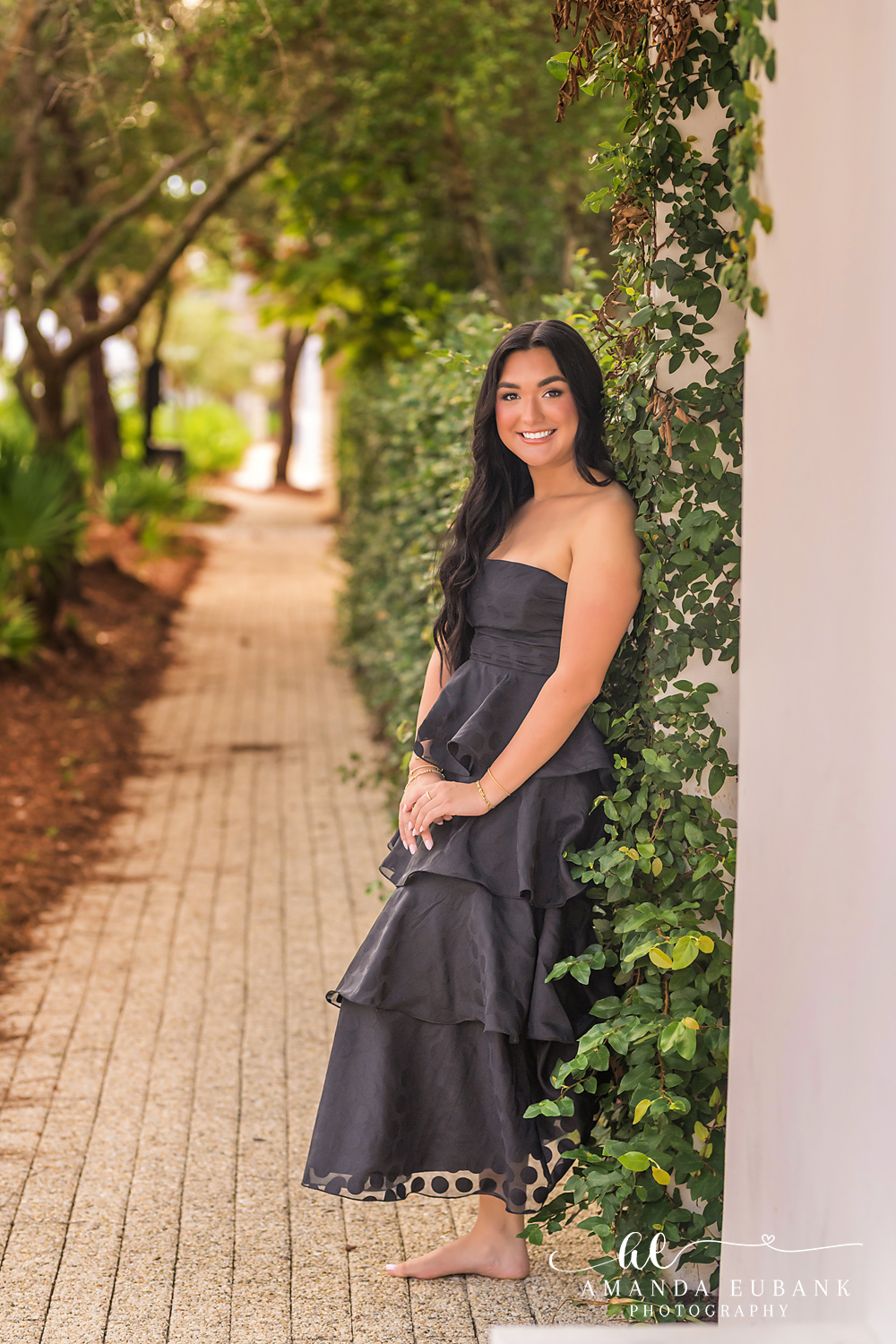 Rosemary Beach Senior Photos | Leaning on an ivy covered wall Rosemary Beach senior photographer: senior girl in a black tiered dress leaning against an ivy covered white wall on a brick path, full length
