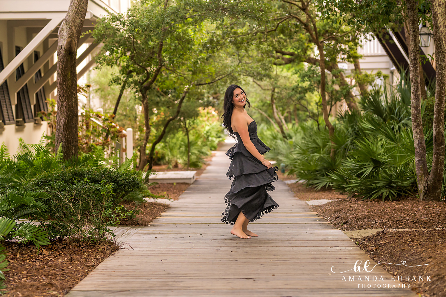 Rosemary Beach Senior Photos | Twirling on a wooden boardwalk Rosemary Beach senior photographer: senior girl twirling barefoot in a black tiered dress on a wooden boardwalk path under live oaks