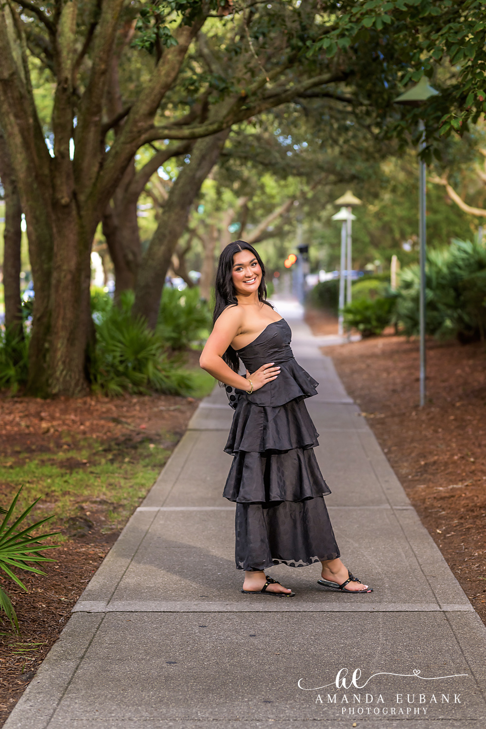 Rosemary Beach Senior Photos | Full length under the live oaks Rosemary Beach senior photographer: full length senior portrait of a girl in a black tiered dress standing on a sidewalk under live oaks