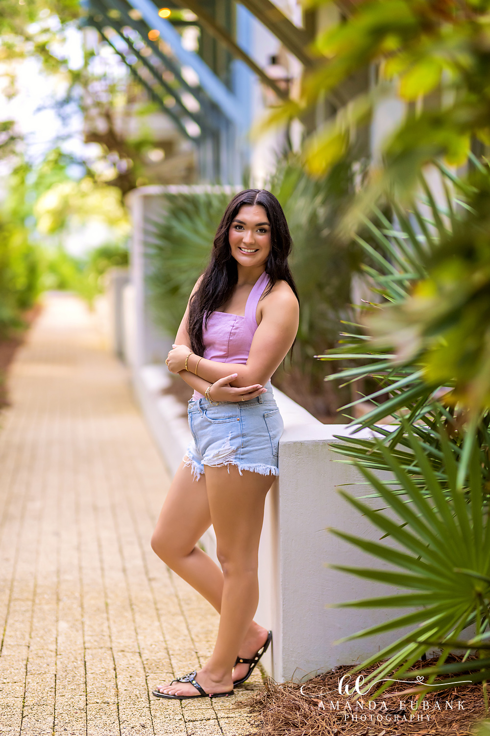 Rosemary Beach Senior Photos | Casual outfit by a white wall Rosemary Beach senior photographer: senior girl in a pink halter top and denim shorts leaning on a white wall beside palm fronds