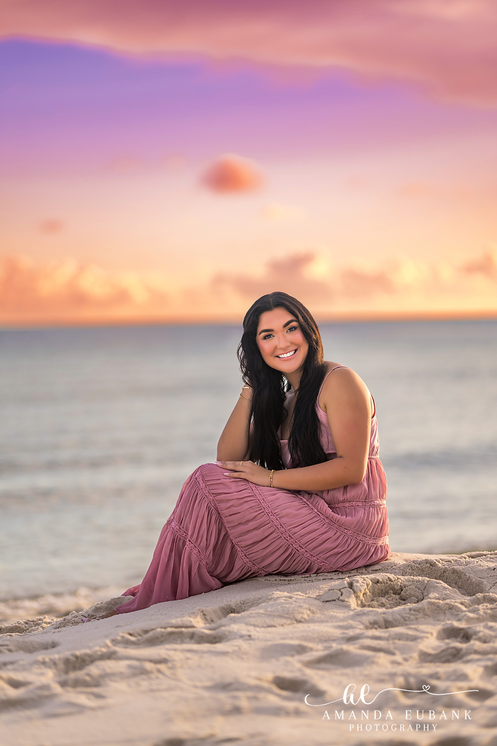 Rosemary Beach Senior Photos | Seated on the sand Rosemary Beach senior photographer: senior girl in a pink maxi dress seated on the sand with the Gulf and a pastel sky behind her