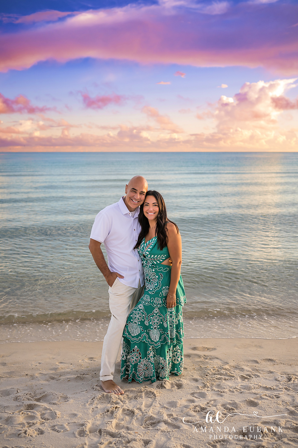 Rosemary Beach Senior Photos | Senior’s parents on the beach Rosemary Beach senior photographer: the senior's parents standing together on the beach, dad in a white shirt and mom in a green floral maxi dress, with a pastel sky over the Gulf