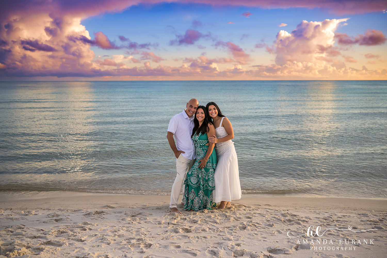 Rosemary Beach Senior Photos | Senior with her parents Rosemary Beach senior photographer: senior girl in a white dress with her parents, dad in a white shirt and mom in a green floral dress, on the beach under a pastel sky