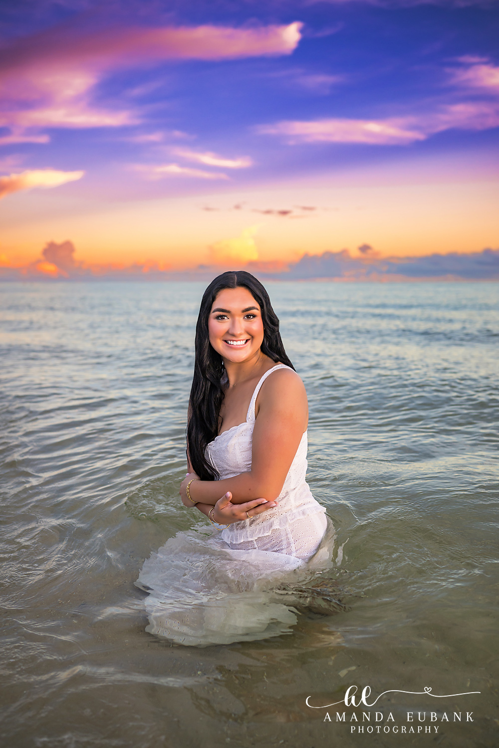 Rosemary Beach Senior Photos | Kneeling in the water Rosemary Beach senior photographer: senior girl in a white dress kneeling in the shallow Gulf water smiling at the camera
