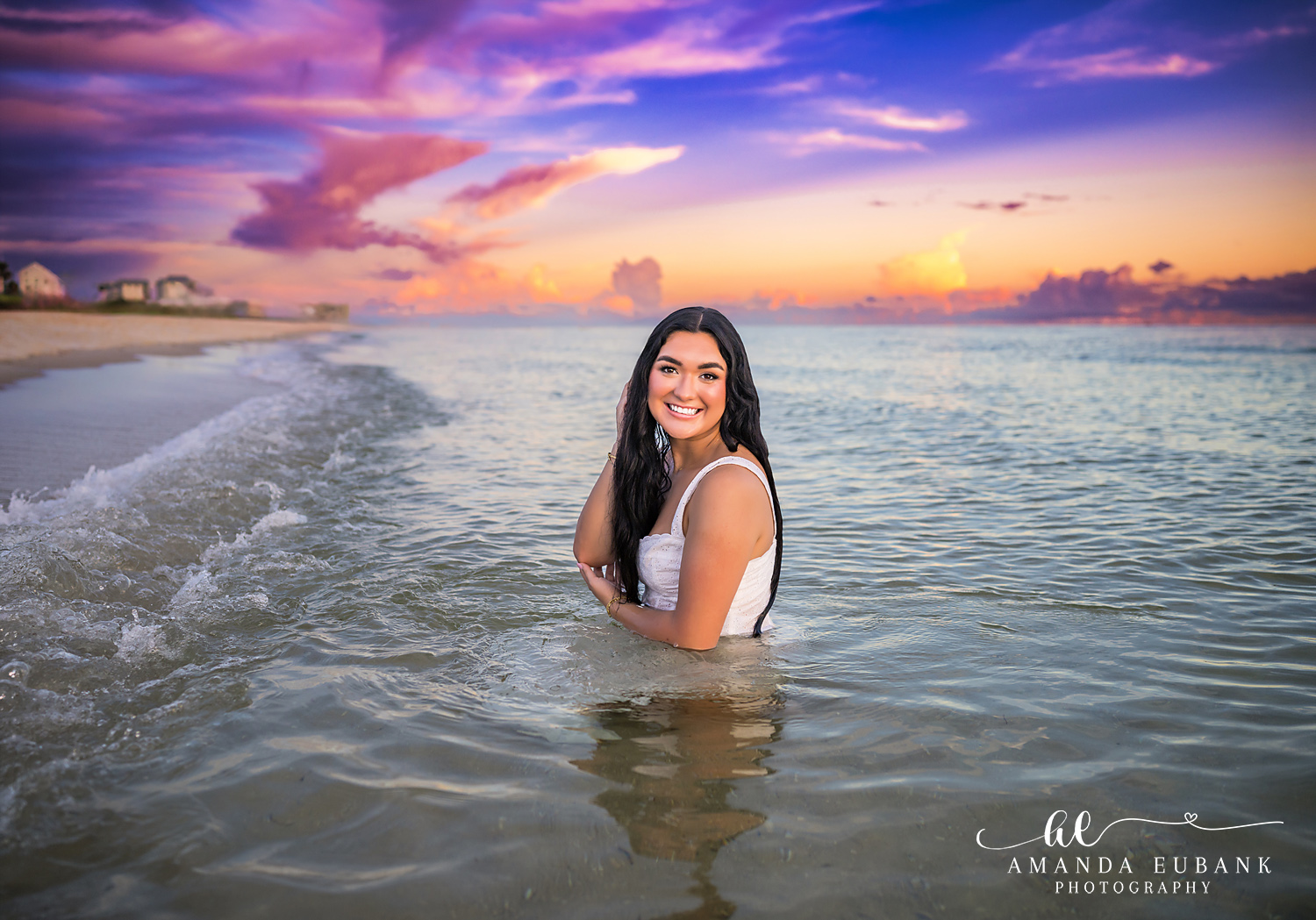 Rosemary Beach Senior Photos | Kneeling in the surf Rosemary Beach senior photographer: senior girl in a white dress kneeling in the shallow Gulf with swirling waves and a colorful sky